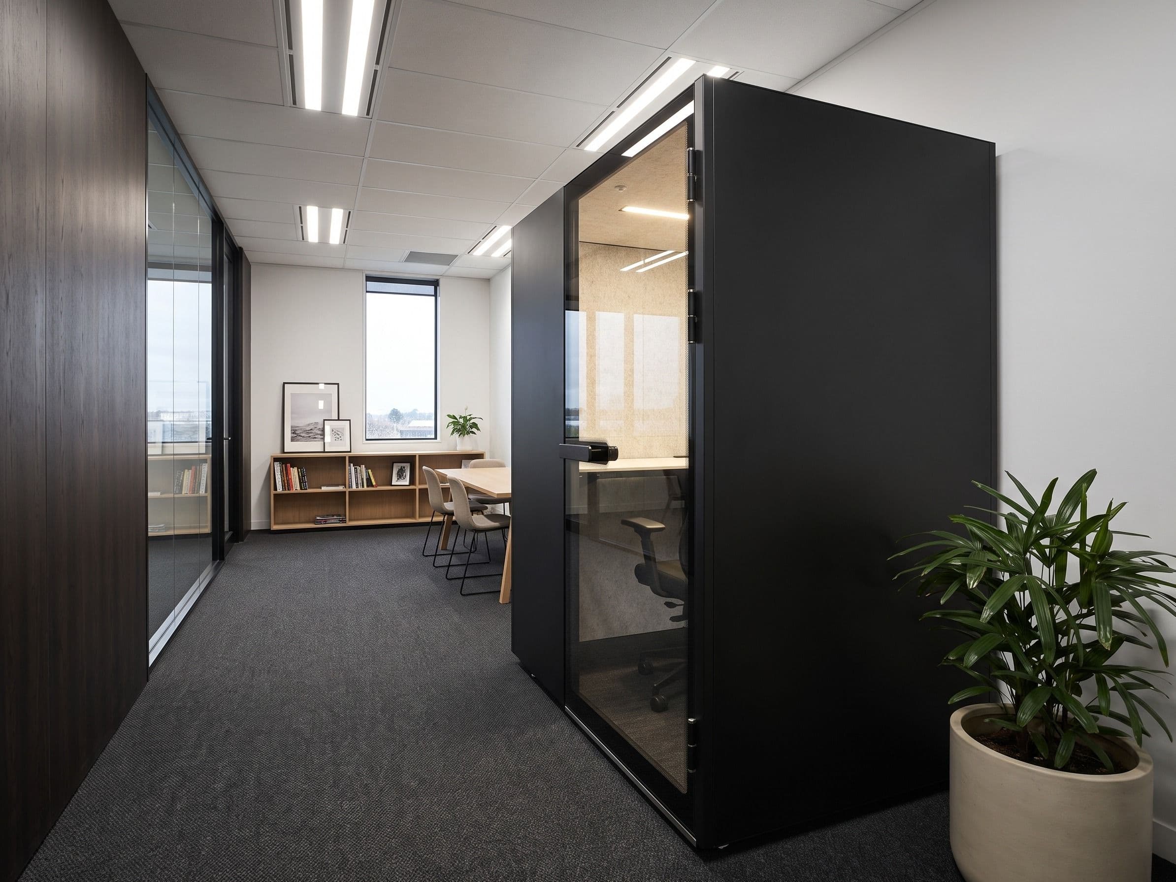 An MW-Pod at the end of an office walkway, seen from one side, with a meeting table and shelving beyond